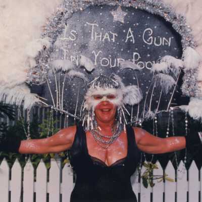 Unknown woman dressed up, her head piece reads is that a gun in your pocket.