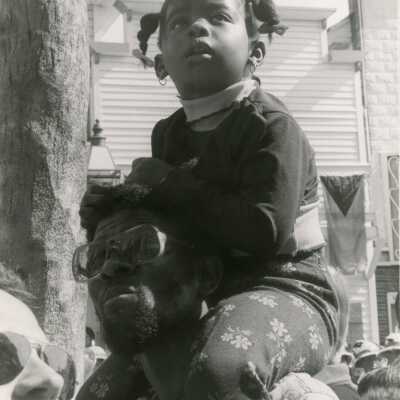 An unknown child sitting on a man's shoulders