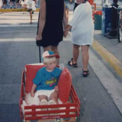 An unknown woman walking with unknown kids, one is being pulled in a wagon.