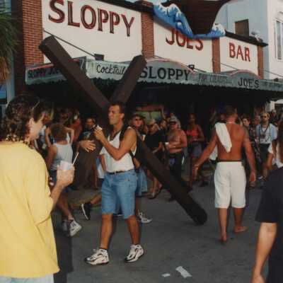 An unknown man carrying a wooden cross in front of Sloppy Joe's Bar.