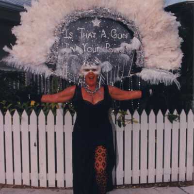 Unknown woman dressed up, her head piece reads is that a gun in your pocket.