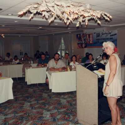 Unknown woman speaking at the podium at the Fantasy Fest meeting.