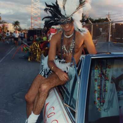 Unknown man dressed up sitting on a car.
