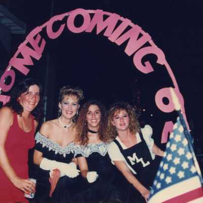 Unknown woman dressed up standing underneath a sign that reads homecoming.