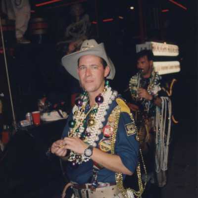 Unknown man dressed up walking next to a float with tons of beads.