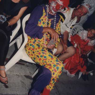 Unknown man dressed as a clown sitting on the side to watch the parade.