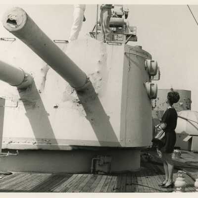 Unknown woman looking on as 2 unknown men in uniform are on top of a machine