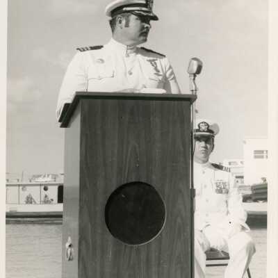 2 Men in uniform, one at the podium