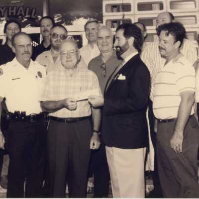 Unknown group of people standing in front of the City Hall. One is accepting a check.