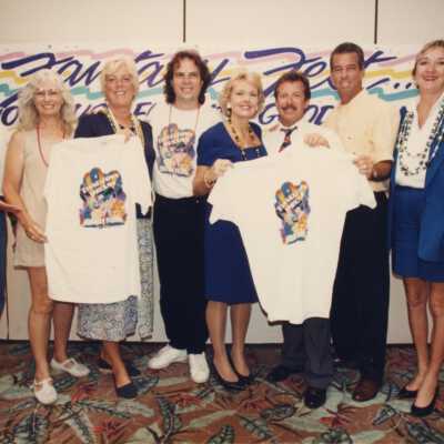 Unknown people standing in front of a Fantasy Fest sign holding T shirts.