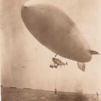 Blimp with Man on Ladder Over Water