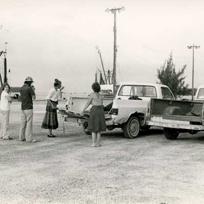 Unknown people standing near 2 trucks and boats in the back ground