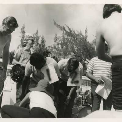Unknown people bending down with a band playing next to them