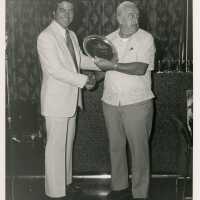 2 Unknown men standing with a plaque