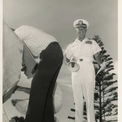 Unknown man in uniform with microphone in his hand and 2 others looking into a box