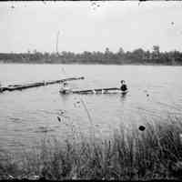          women with dock.jpg 667KB; Two women in the water with an overturned rowboat. A pair of feet are visible under the boat. The crack in the image suggests the originals were from glass plate negatives.
   