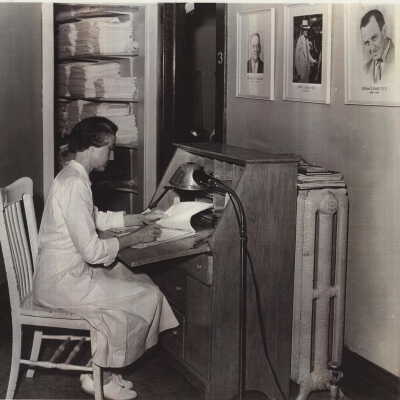 LoisCorkhillDouglas_Hosp: Same photo of Dr. Corkhill on the wall. The seated woman is Lois Corkill, Dr. Corkill's spouse. She continued to serve the Douglas Community hospital.
