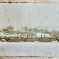          log slide: cut pine logs waiting for the spring melt-flood to carry them downriver to the lumbering mills.; May be Purdy's Riverside Farm in the distance.
   