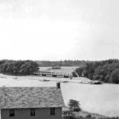 Bridge + dredge 1936.jpg 1.2MB: https://sdhistoricalsociety.org/Newsletter/2011/nov11/nov11_newsletter.htm

The Bridge and The Bridges by Jack Sheridan

I often think of this photo as I drive from Saugatuck to Douglas over this causeway, looking out on the river and down on the turtle pond and condos perched on what was once the road. The sandsucker in the photo lying out on the water was a monster machine that sucked silt off the river bottom and pumped it through floating pipe to create much of the fill you see. The structures on the right are the Twin Gables Hotel – still with us today.

Seventy five years later, now we drive on top of the causeway and sit on it while awaiting the green light to cross on the single lane to Douglas due to the bridge rebuilding. A good time to remember the history.

Depending on how you define bridges there have been a number of them between Saugatuck and Douglas. The first was located in Saugatuck where the chain ferry crosses now. The next was fifty yards north of where it is today and of course the present freeway bridge to the southeast. The photo was taken in the summer of 1936 and at that time this causeway was the biggest fill project in the whole State. The new bridge was under construction to the left and not visible in this photo. The bridge and causeway replaced the 1901 bridge that was actually two bridges. On the Saugatuck side and visible in this photo is a steel truss bridge. Small boats could pass beneath it but the water was probably shallow. Then there was a causeway of maybe a hundred yards leading to the main bridge which was a swing bridge over the deep channel. It was about seventy feet in length and pivoted on a piling in the middle of the channel. It was opened with a geared lever powered by an attendant who lived in a house next to the bridge.