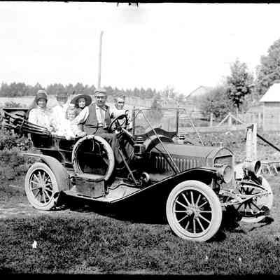 Sim Old car A.jpg 672KB: Roger Reed behind the wheel of a loaded Model T-style automobile with a farmyard in the background.