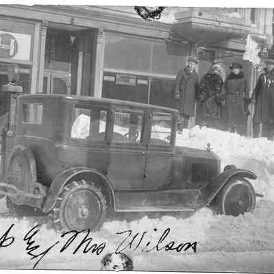 89-1-274_Capt._Mrs._Wilson.jpg 632KB: Captain William P. Wilson 1861-1940 and wife stand on a snowbank beside a city street. In the foreground a car awaits with chains on the tires.