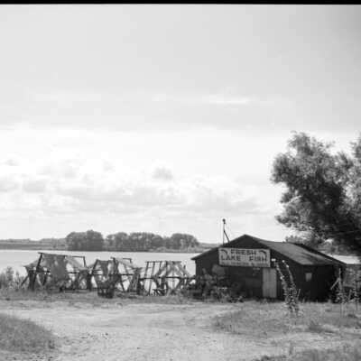 369 GeorgeSewersShanty at Culver Street - site is now Coghlin Park: # 369 This is the Sewers fish house east of the Blue Star Highway and north of the Blue Star bridge. It burned in the 1970s. In the background is a distinctive row of trees south of the river where there used to be a quonset shaped boathouse.
Source: SDHS newsletter pg 238