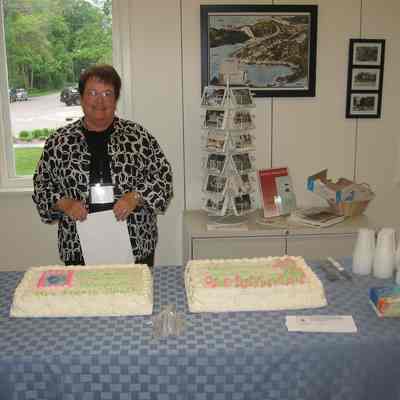 IMG_9859.JPG 999KB: Peg Sanford ready to serve cakes decorated with the messages "In honor of our storyteller May Francis Heath" (at left, with photo) and "Writer * Teacher * Artist * Civic Leader"