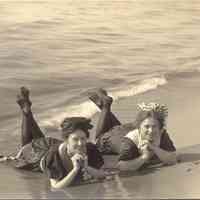          02.TwoLadiesLieonSaugBeach1910.jpg 101KB; Two women lay on the beach, in the shallows, their heads raised on their elbows and their ankles crossed. The two ladies are wearing dark swimming attire and stockings. The two girls are smiling.
   