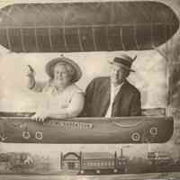          04.BalloonEyeViewofTown.SUPER!!!.jpg 100KB; A man and a woman in a photo background that look like they are in balloon floating over Saugatuck landmarks the Coral Gables (then Hotel Saugatuck), Big Pavilion and Hotel Butler. A sign by her arm reads 