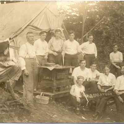 021.HardCoreCampersSaug.jpg 129KB: Eleven man and boys pose with their tent that is furnished with an iron stove.