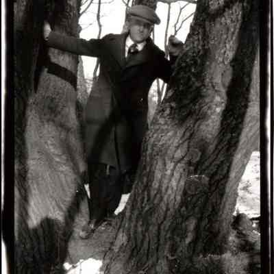 95-52-1a_man unknown.jpg 240KB: Man in a long coat standing in a gap between two trees.