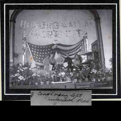 HH-CongregationalChurch.jpg 1.1MB: Photo of four women on a stage decorated with vases and pots of flowers. A USA flag is hung across the back wall and vine-adorned letters over head spell out "Honors Wait at Labor's Gate" overhead. One woman is seated at a piano.