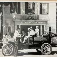          Saugatuck City Hall with Officer Henry Hungerford and car driven by Harold Whipple.; Newspaper prints of the photo identify the driver as Willard Prentice, see 2024.13.19
   