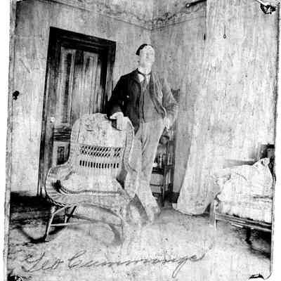 89-1-54B Geo Cummings.jpg 626KB: Young man standing in a parlor with elbow on a wicker chair