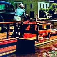          man cranking chain ferry to transport car across river
   