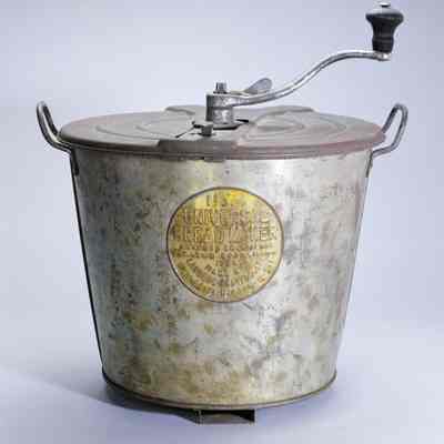 Universal Bread Maker complete, photo from https://upload.wikimedia.org/wikipedia/commons/4/4c/Universal_Bread_Maker.jpg: "Manually-operated, tabletop dough mixer, kneader and raiser; makes up to 4 loaves. Consists of a tapered circular container, made in three pieces with two folded, vertical seams and bottom folded up at edge, that has two side handles curved inward above its heavy, rolled rim and a shallow slot attached on bottom underside for a separate clamp that secures device to table or horizontal support; a stamped, Y-shaped crosspiece that snaps over the rim and has a central circular bearing to hold the dough hook and curved crank with black-painted wooden knob; and a cover placed on top of the crosspiece, stamped with instructions in raised sans serif letters. Assembly held together by turn latches. Crosspiece bears product name above two columns of patent dates from 1900 to 1906 and maker information, all in incuse letters; product information with "AWARDED GOLD MEDAL / ST. LOUIS EXPOSITION" are embossed inside a large circle on container side."
Description from https://americanhistory.si.edu/collections/nmah_309749