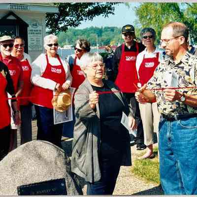SDHS volunteer tour guides wearing their red aprons for a ribbon cutting cerimony: Ron Hirsch, George and Dawn Schumann, possibly Ken Gold, Harold Thieda, Kathleen Markland, Merle Malmquist, Kit Lane, unknown man with black hat, Dottie Lyon, and Jeff Spangler
