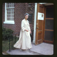          Page E, 9. Woman standing outside Woman's Club with notice for Centennial Tea
   