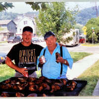          11. Color photo of a young man and John C. Diepenhorst standing in front of a rack of smoked fish. 700 block of Water Street visible in background including Jim Sewers boat barn and the Star of Saugatuck building. Circa mid 1980s to 1990s
   