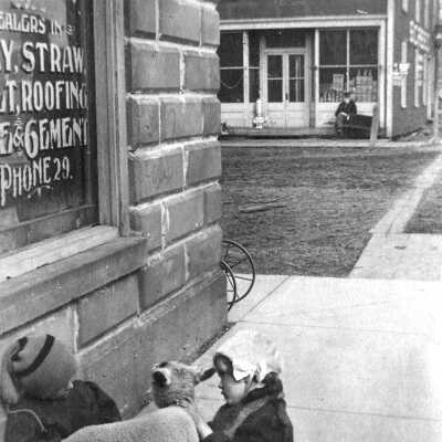 THE YOUNG AND THE OLD ca. 1904 Culver and Griffith Streets Saugatuck Changing environments, changing generations. Children at play in front of Roger Reed’s new feed and livery store, constructed of modern concrete block and with concrete sidewalks—being watched by an old man across the street in front of Roger’s father’s store, with its old fashioned wood front and wood sidewalk.: filename: LO68 SC Reeds Livery 03.26A