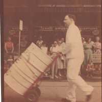 Man in white garb pushing drum on cart