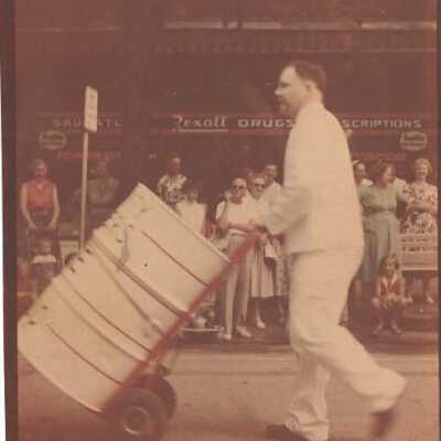Man in white garb pushing drum on cart