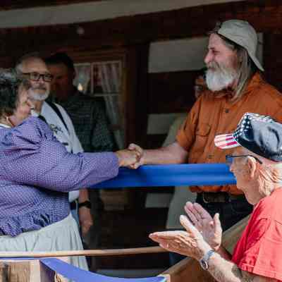 Diana Peyton shaking hands with Michael Bailey 1835 Barker Family Log Cabin front porch before ribbon cutting