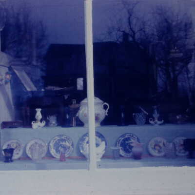 Window display with fine china plates and tea pot. Desk visible in the background