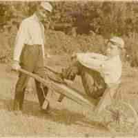          Boy pushing another boy in a wheelbarrow
   