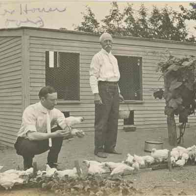 Inscription: Brooder House. This House is 15 feet deep and 24 feet long, divided into 6 divisions for 50 chicks in each division with heated brooders to keep them warm. The crouching man is Mr. Moore, who spent the 4th with us.