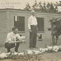          Inscription: Brooder House. This House is 15 feet deep and 24 feet long, divided into 6 divisions for 50 chicks in each division with heated brooders to keep them warm. The crouching man is Mr. Moore, who spent the 4th with us.
   
