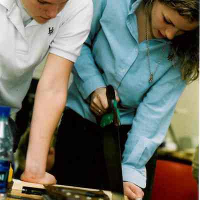 Two students work together to saw a board.