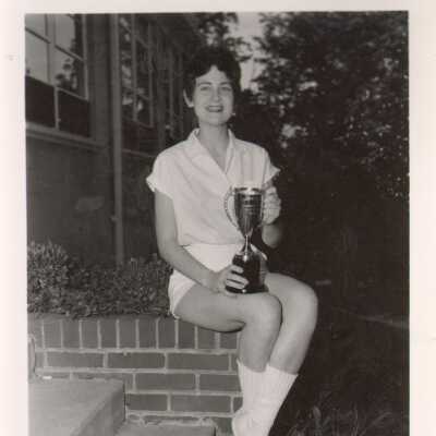Student in athletic uniform poses with trophy, 1960s