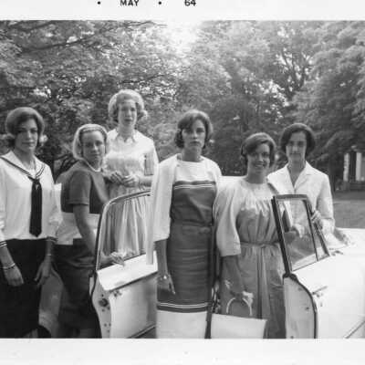 Six students in dress clothes standing in front of a white convertible in 1964.